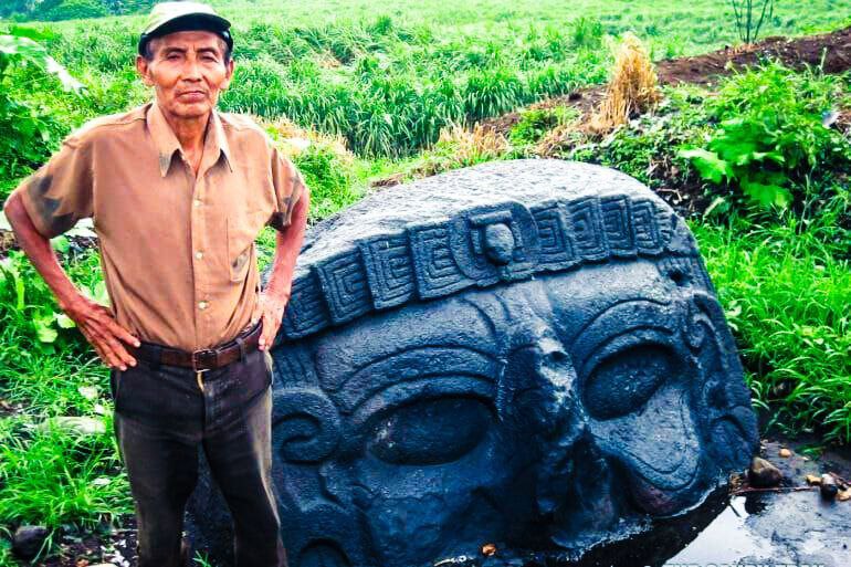 De uitdrukking en jukbeenderen van de rietwerker lijken opvallend veel op het gigantische stenen gezicht van deze surrealistische voorouder.